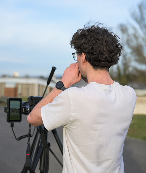 Photo de Yanis Oberlé de dos, devant une caméra posée sur trépied. Crédit: Manon Egmann